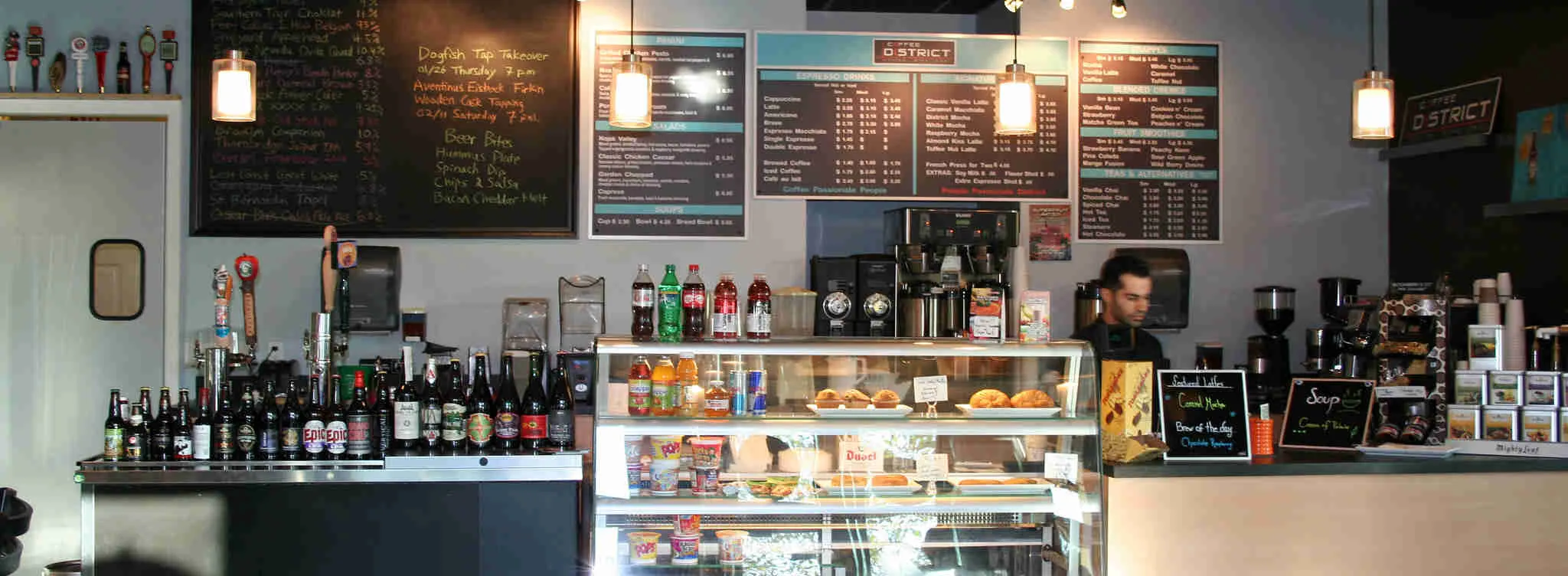 Theke eines Coffeeshops/Imbiss mit Getränken und Snacks in der Auslage. Liste mit angebotenen Speisen und Getränken im Hintergrund